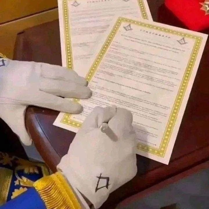 Main gantée signant un document orné de l'équerre et du compas